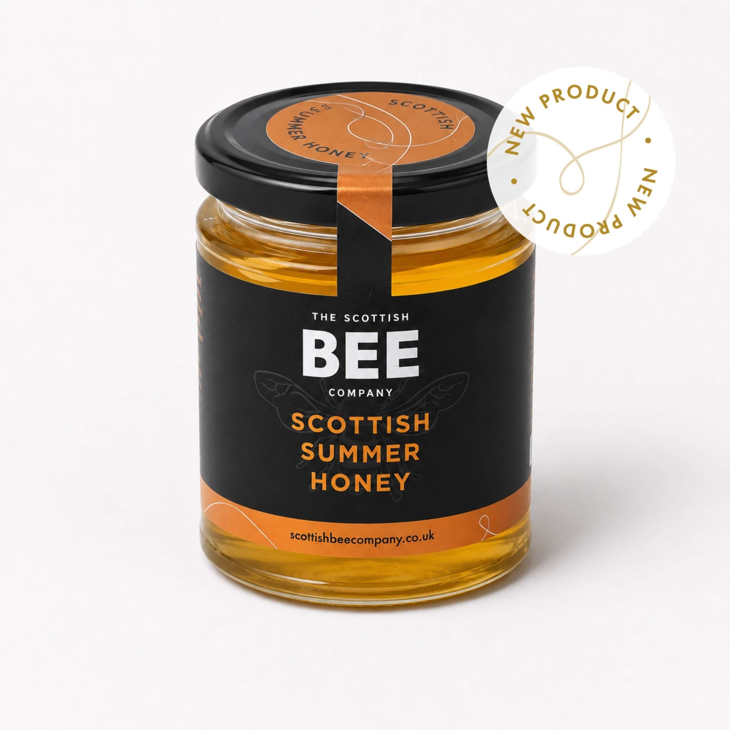 A glass jar of Scottish Summer Honey by The Scottish Bee Company, featuring a black label with orange accents and a black lid. A white circular badge on the top right reads &