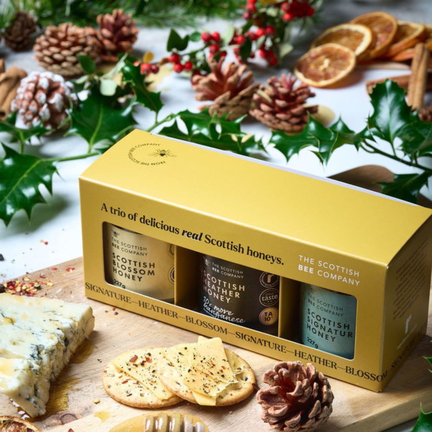 Yellow box of Scottish honey with honeycomb and honey dipper on a festive background. Includes Scottish Blossom Honey, Scottish Heather Honey and Scottish Signature Honey