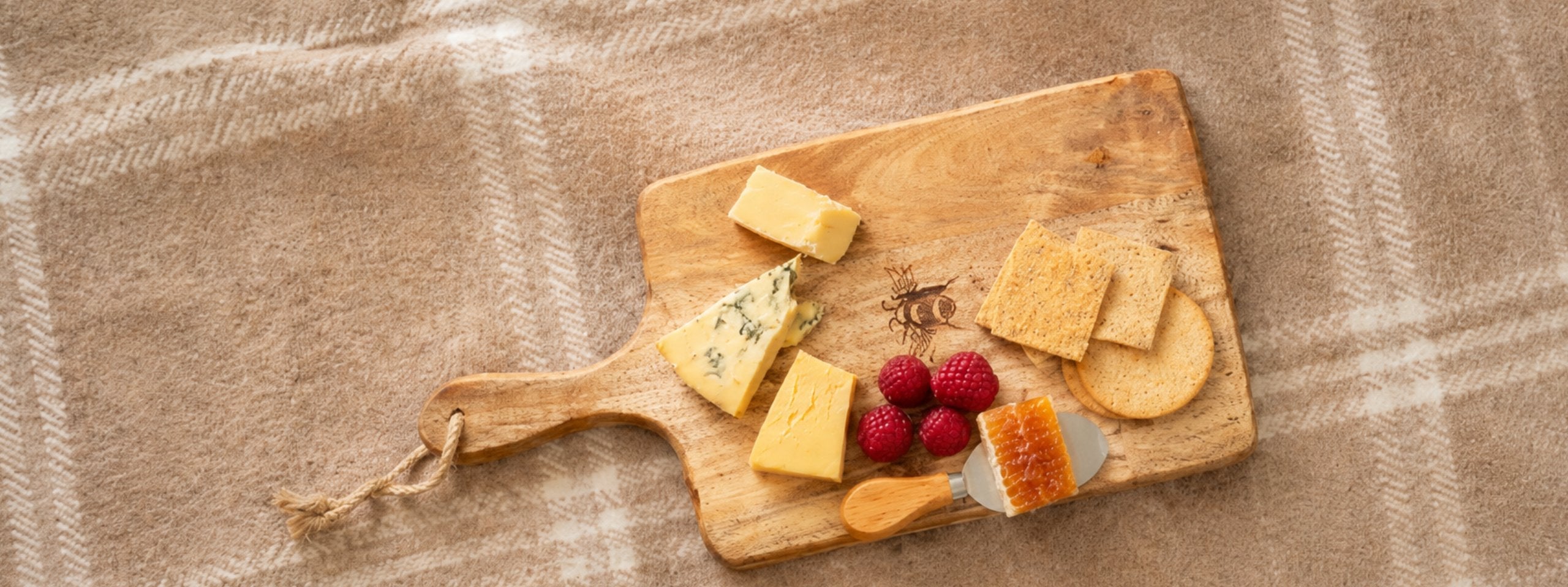 scottish bee company cheese board with honeycomb, cheese and fruit on it on a plaid blanket