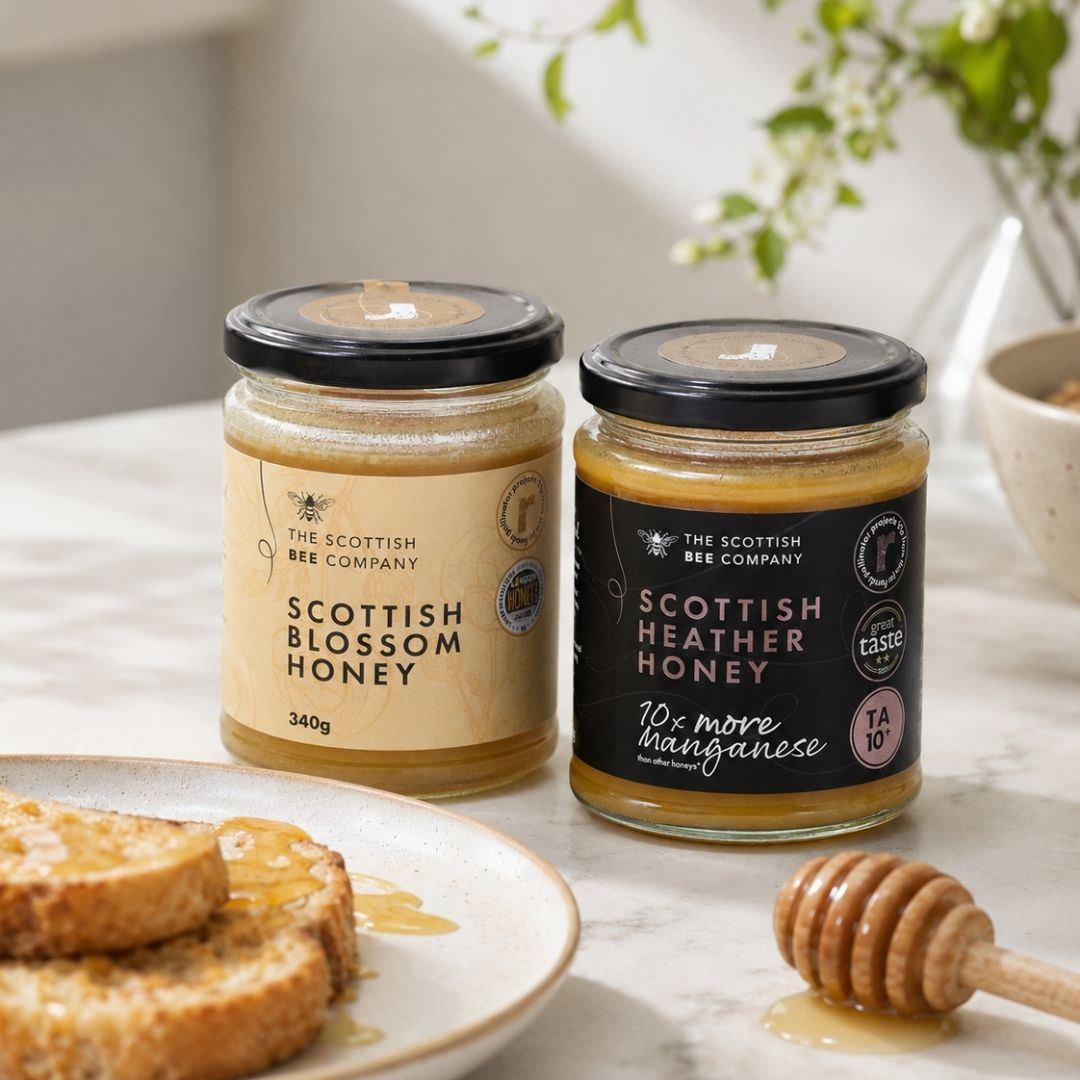 Two jars of Scottish honey on a table with toast and a honey dipper.