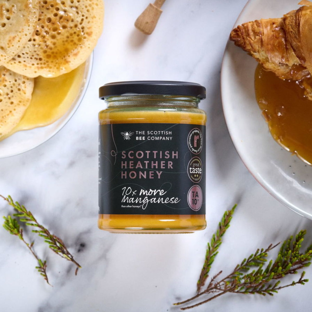 Jar of Scottish Heather Honey with pancakes and croissant on a marble surface