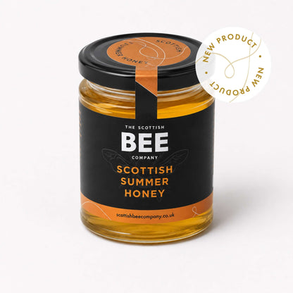A glass jar of Scottish Summer Honey by The Scottish Bee Company, featuring a black label with orange accents and a black lid. A white circular badge on the top right reads &