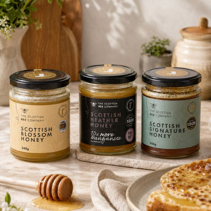 Three jars of Scottish honey on a table with a plate of food and flowers.
